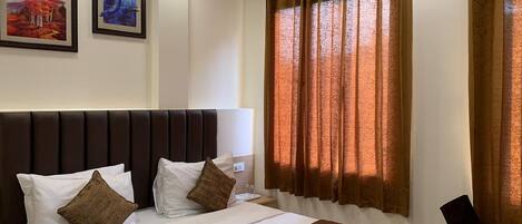 A hotel room with a large bed, a headboard, two pillows, a remote control, a chair, and curtains.