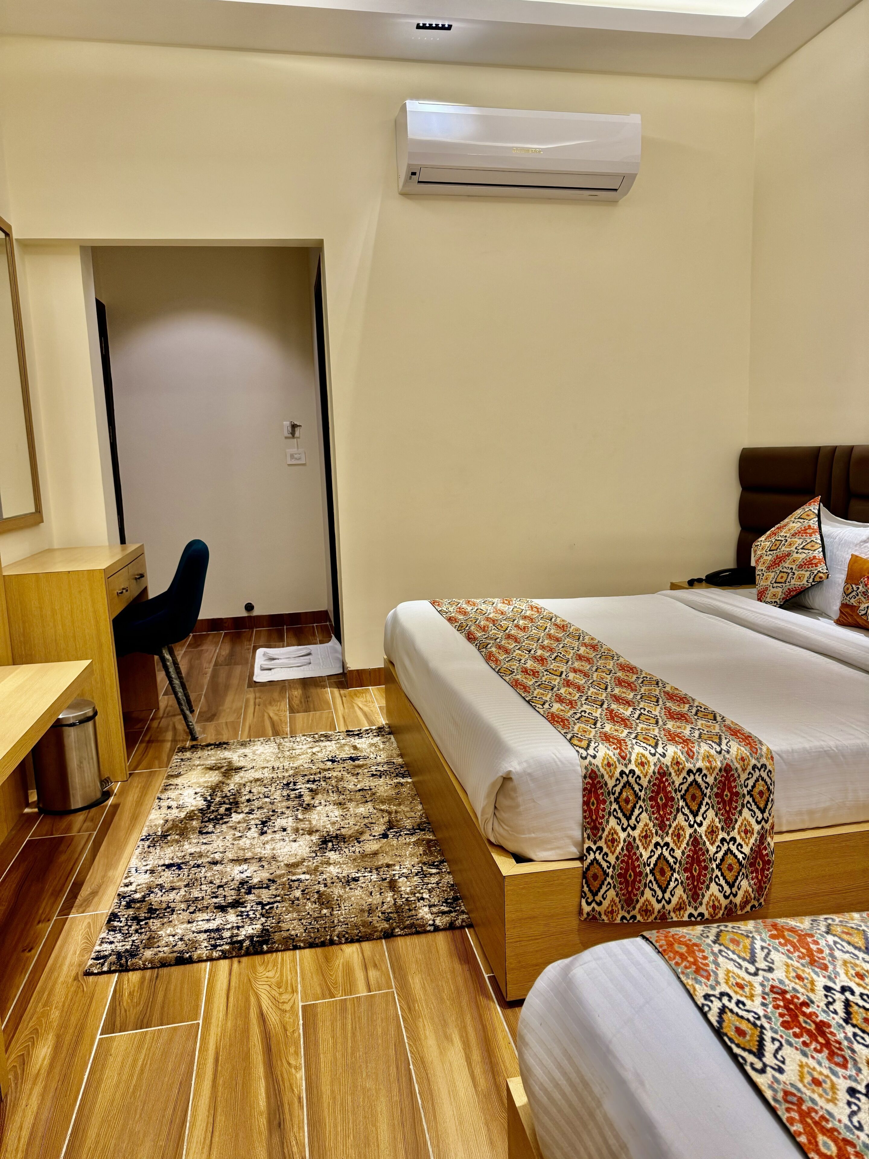 Habitación de hotel con cama, escritorio, silla, equipo de aire acondicionado y alfombra estampada.