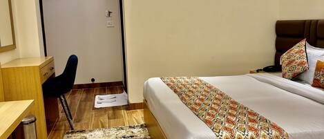 Habitación de hotel con cama, escritorio, silla, equipo de aire acondicionado y alfombra estampada.