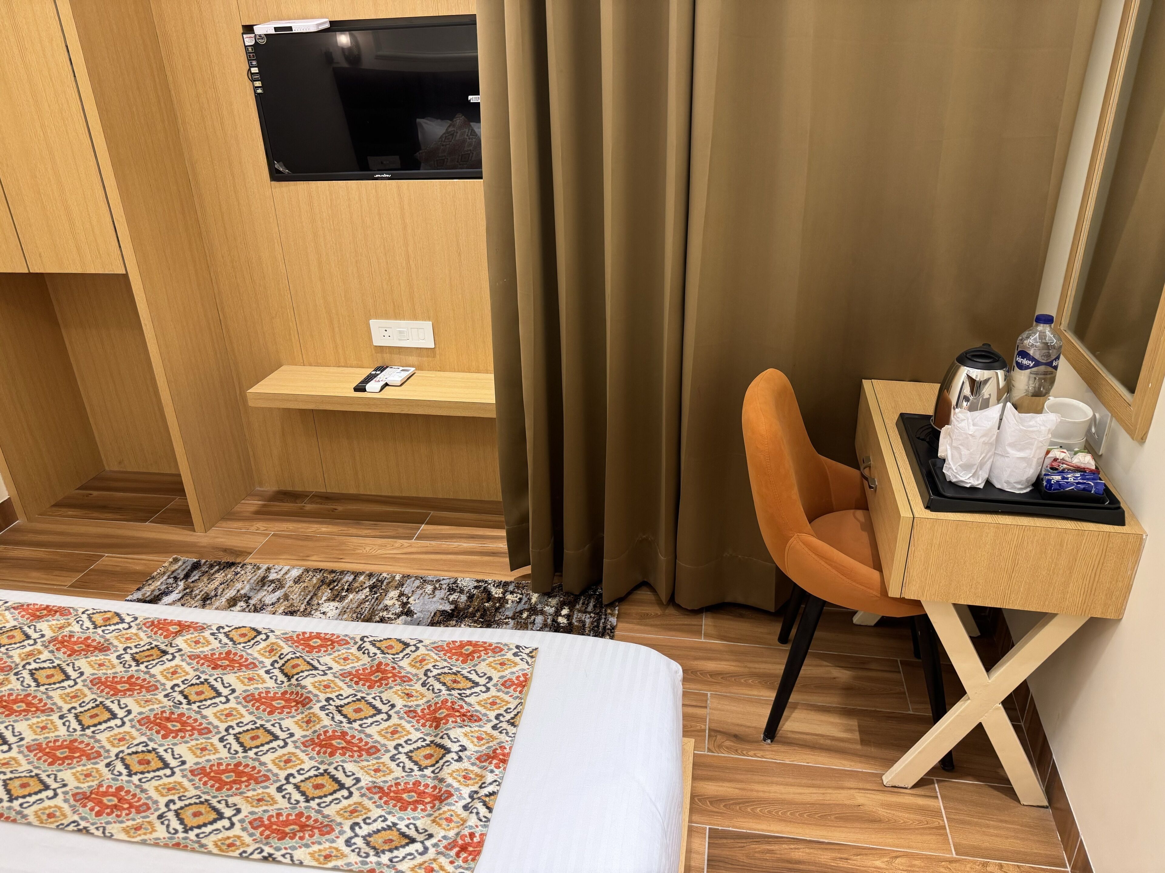 A hotel room with a bed, a desk with a tray of toiletries, a TV, and a window with curtains.