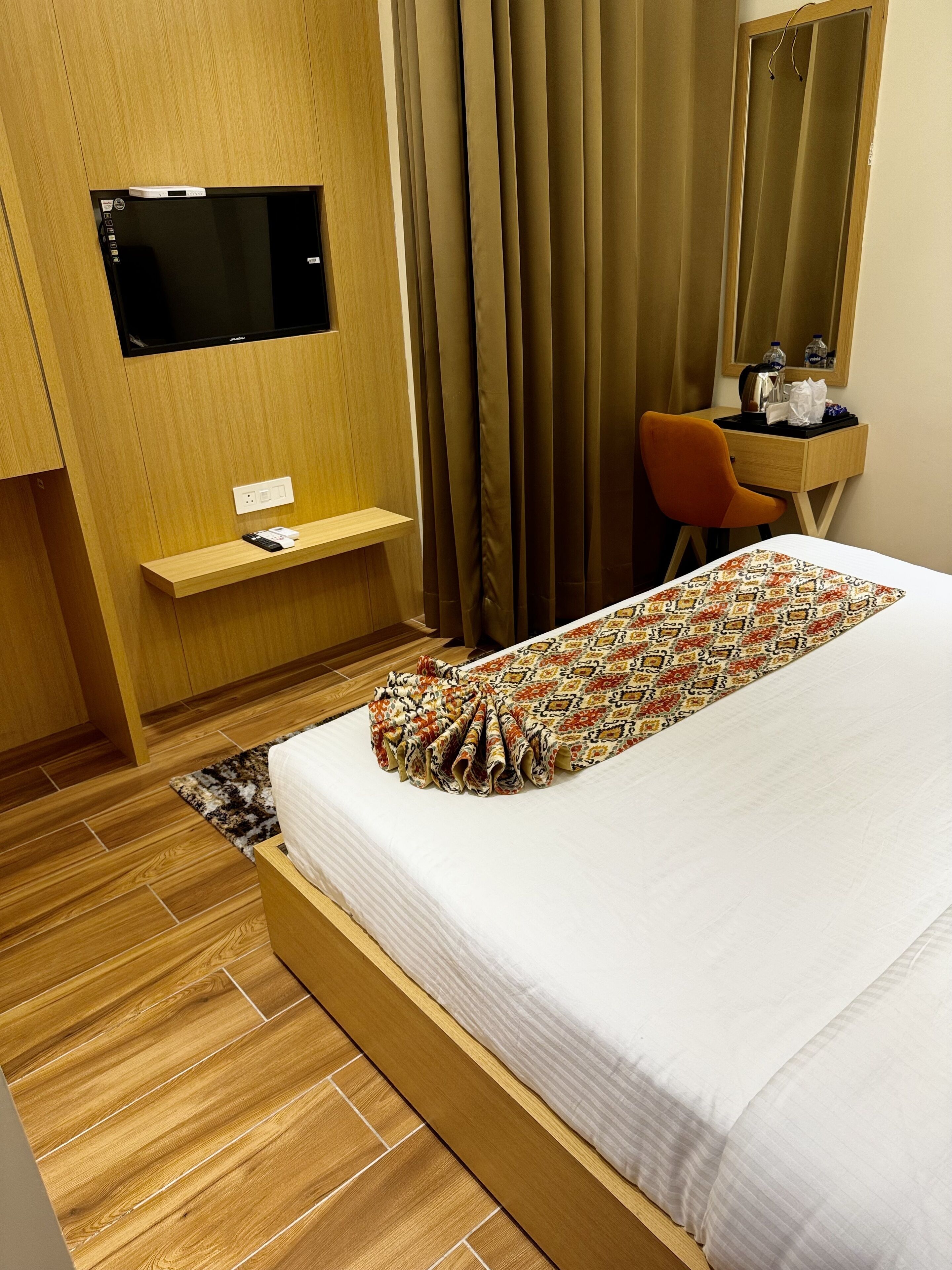 Habitación de hotel con cama, escritorio, silla, televisor y ventana con cortinas.