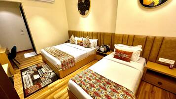 A hotel room with two beds, wooden flooring, a wall-mounted air conditioner, a small table with a lamp, and a decorative mirror.