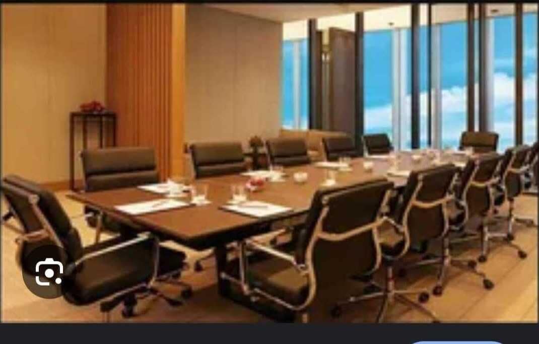 A conference room with a long table, multiple chairs, and a view of the sky through large windows.