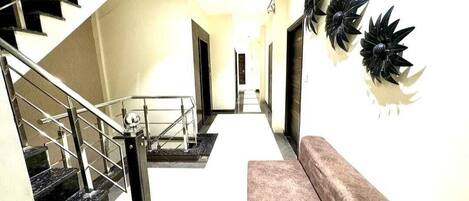 Una escalera con barandillas metálicas que conduce a una plataforma con una pared color beige y un sofá marrón.