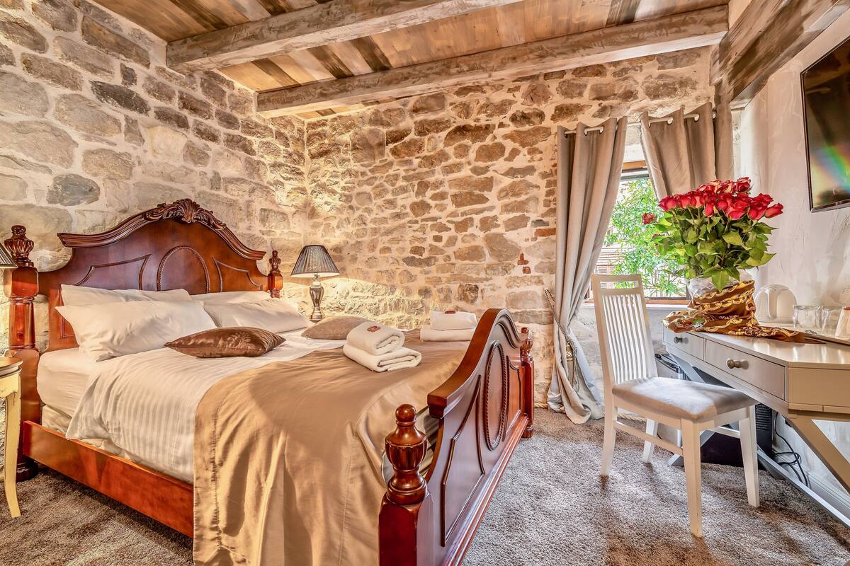 A stone-walled bedroom with a wooden bed, a desk, and a chair.
