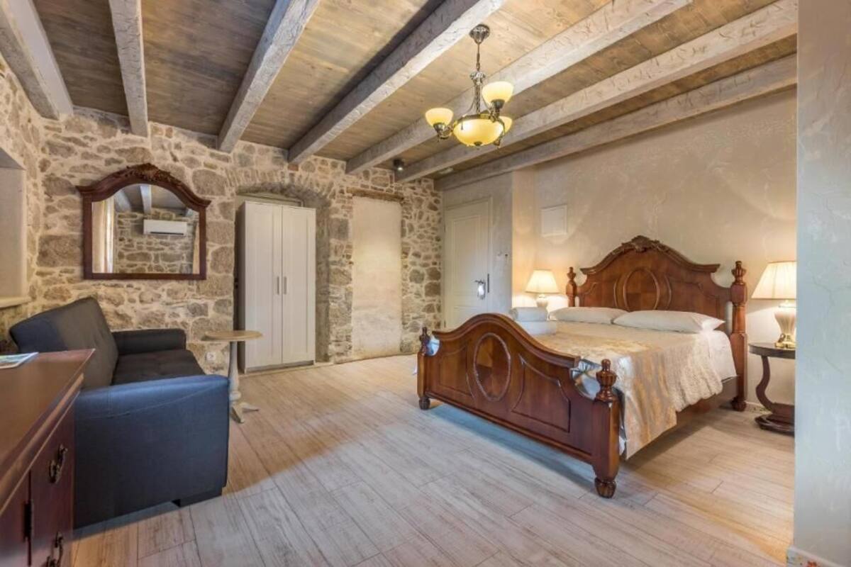 A bedroom with a wooden bed, stone walls, a stone fireplace, a desk, and a chair.