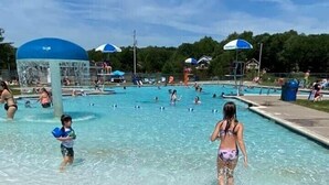 Zona de piscina con agua cristalina, marcadores flotantes amarillos y sombrillas.