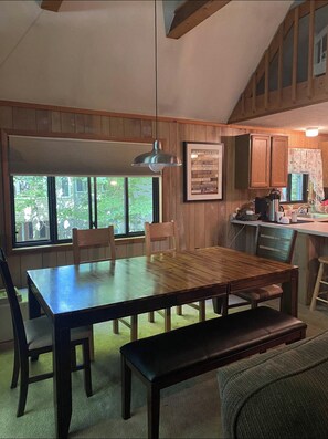 A cozy kitchen with wooden cabinets, a dining table with chairs, and a large window providing a view of greenery outside. - Pocono retreat, arrowhead lake beautiful chalet  (Pocono lake)