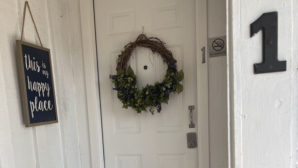 Una puerta blanca con un adorno de navidad, un cartel de 'no fumar' y un número '1' en la pared.