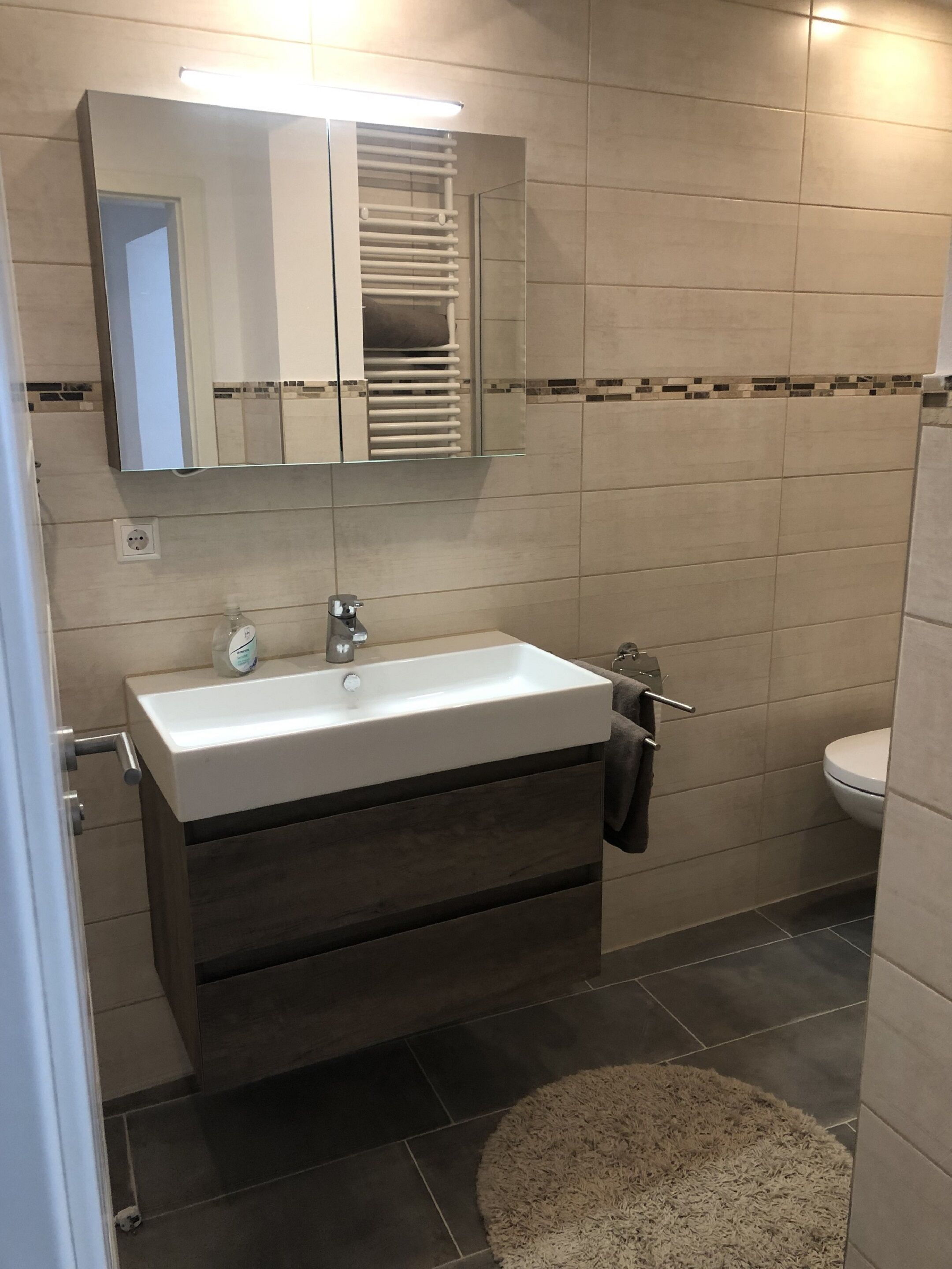 A modern bathroom with a rectangular sink, a mirror above it, and a towel rack.