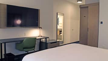 Habitación de hotel con cama, escritorio, silla, espejo y armario.