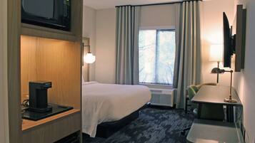 A hotel room with a bed, a desk, a coffee maker, a TV, and a window with curtains.