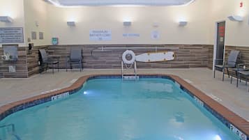 An indoor swimming pool with clear safety signs, a lifeguard chair, and a maximum bather load sign.