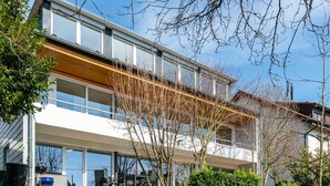 Un bâtiment moderne à plusieurs étages, doté de grandes fenêtres, d’un espace extérieur couvert et d’un jardin bien entretenu.