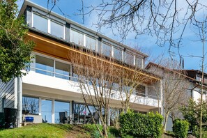 Ein modernes Mehrgeschosshaus mit großen Fenstern, einem überdachten Außenbereich und einem gepflegten Garten.