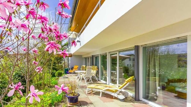Une maison moderne dotée d’un patio, de mobilier d’extérieur et d’un jardin agrémenté de fleurs roses.