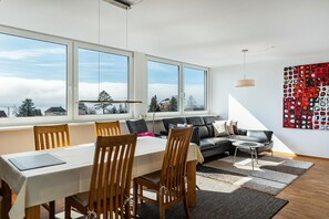 Ein modernes Wohnzimmer mit Essbereich, großen Fenstern, einer Couch und einem Wandbild.