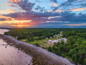 A coastal area with a beach, forested hills, and a small cluster of houses with a clear path leading through the trees.