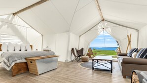 Alojamiento en tienda de campaña con cama, zona de estar y vistas al mar.