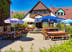 An outdoor seating area with wooden tables and benches, surrounded by potted plants and umbrellas. - Gasthof Zur Altmühlquelle (Windelsbach)