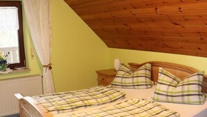 A wooden bed in a room with a sloped ceiling and a window with curtains. - Gasthof Zur Altmühlquelle (Windelsbach)