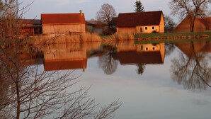 A calm lake reflecting buildings and trees. - Gasthof Zur Altmühlquelle (Windelsbach)