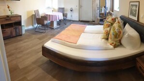 A bedroom with a curved bed, a bedside table, a chair, a small table with a lamp, and a window. - Hotel Zur Igelstadt (Lichtenfels)