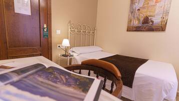 A hotel room with a single bed, a wooden headboard, a nightstand with a lamp, and a painting on the wall.
