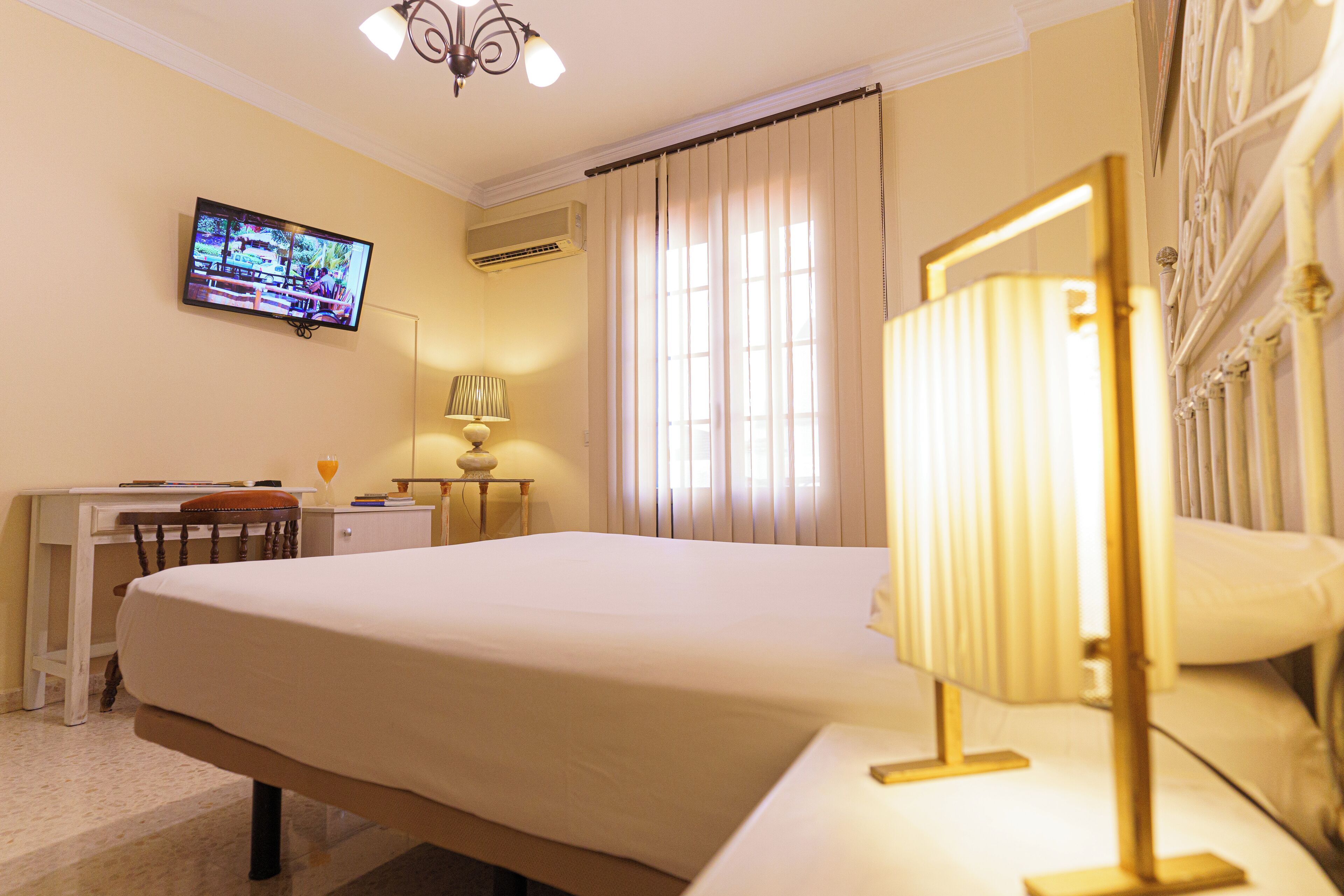Habitación de hotel con una cama grande, un escritorio con silla, un televisor montado en la pared y una ventana con cortinas.