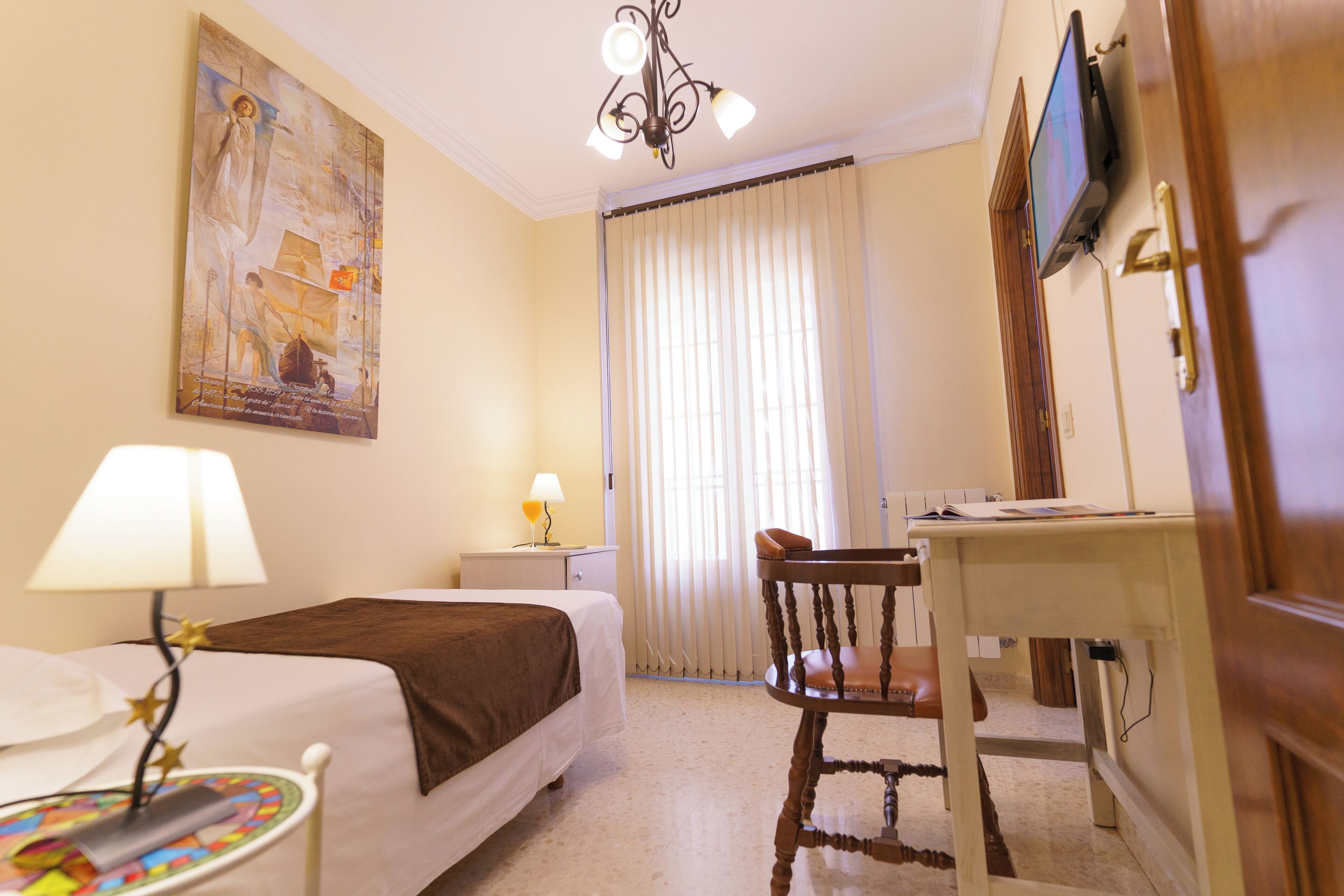 A hotel room with a bed, a desk, a chair, a television, and a painting on the wall.