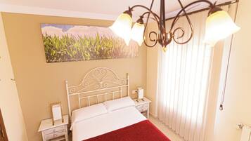 A bedroom with a bed, nightstands, a red throw blanket, a wall-mounted picture, and a ceiling light fixture.