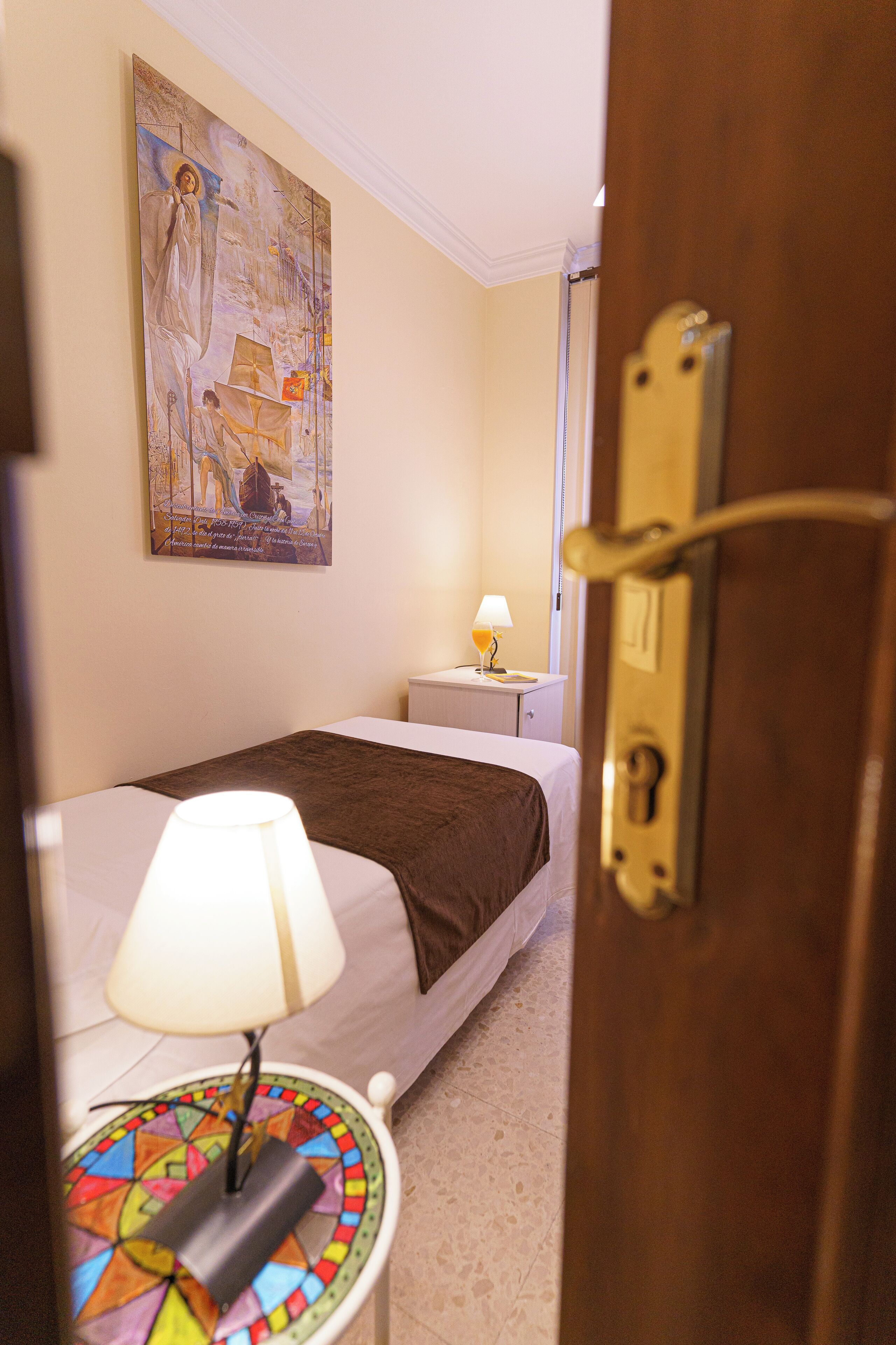 Una habitación de hotel con una cama, una mesita de noche, una lámpara y un cuadro en la pared.