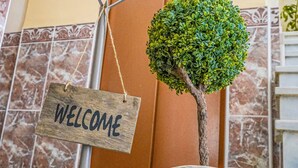 A welcome sign, a small potted tree, and a woven basket in front of a door. - Hotel Colón (Ronda)