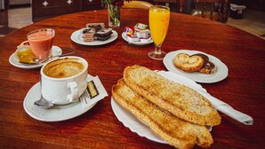 A dining table with a coffee cup, a glass of orange juice, and bread. - Hotel Colón (Ronda)