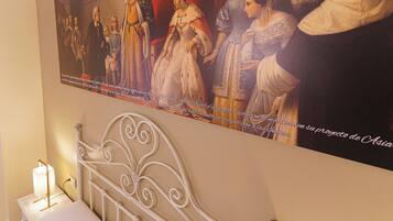 Pintura de figuras históricas en una pared sobre una cama con cabecera de metal.