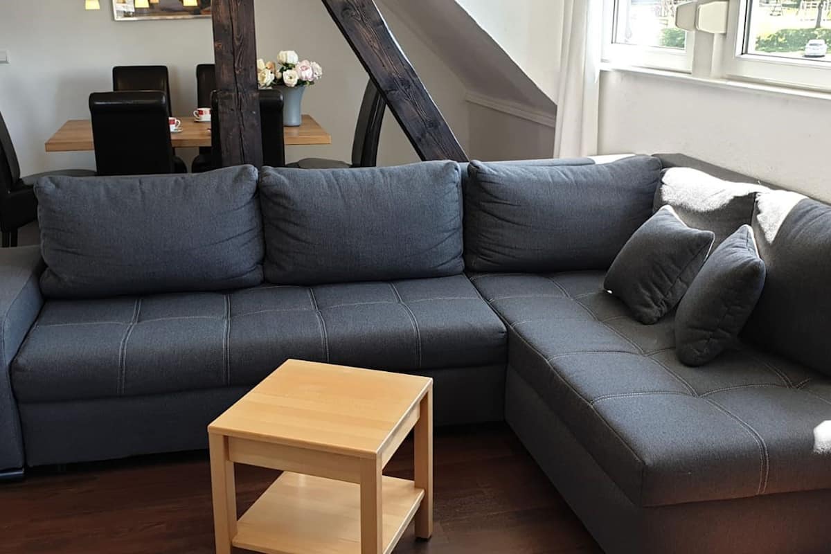 A modern living room with a grey sectional sofa, a wooden coffee table, and a dining area with a table and chairs.