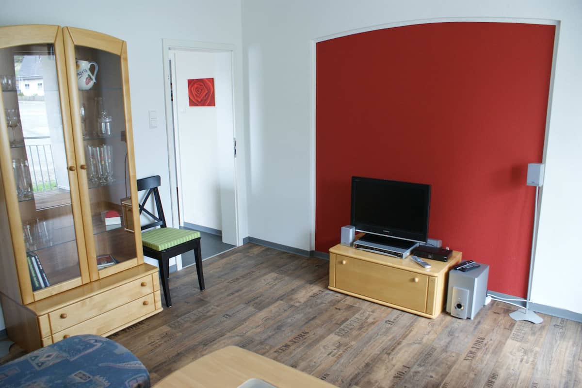 A compact living space with a wooden cabinet, a television on a stand, and a red accent wall.