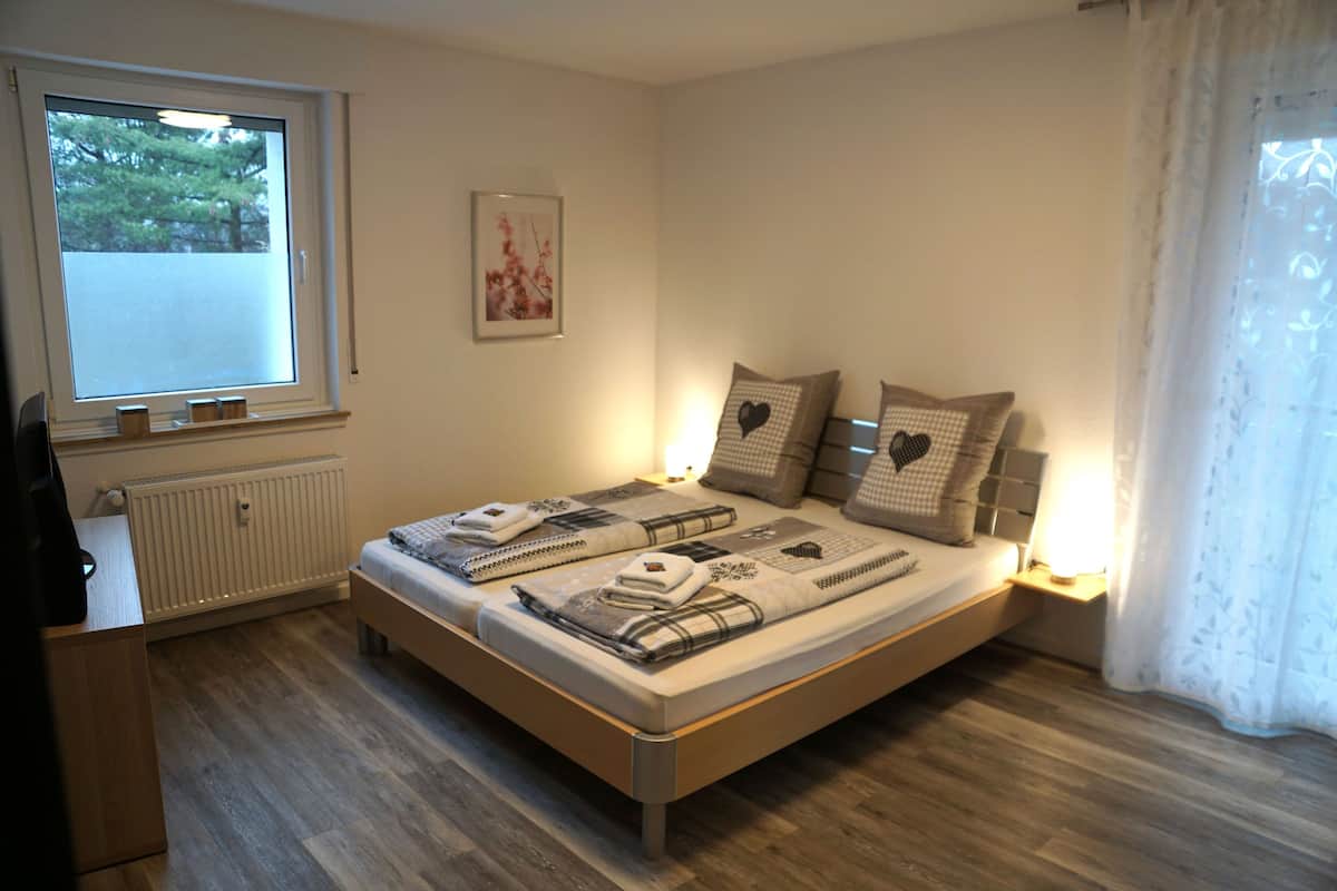 A bedroom with a bed, a radiator, a window, and a wall-mounted picture.