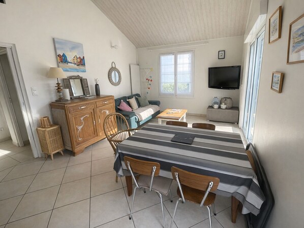 A room with a dining table, chairs, a sofa, a TV, and a window.