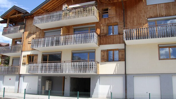 A multi-story wooden building with balconies, large windows, and garage doors.