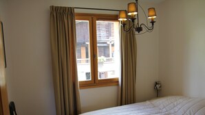 A bedroom with a bed, a window with curtains, and a chandelier.