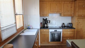 A kitchen with wooden cabinets, a Bosch oven, a sink, and a window with blinds.