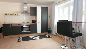 Una cocina moderna con estufa, horno y armarios, un taburete de bar y una ventana con cortinas.