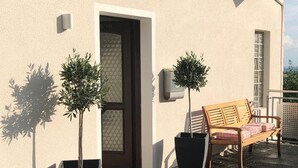 Un edificio con fachada color beige, una puerta de madera y dos plantas en macetas.