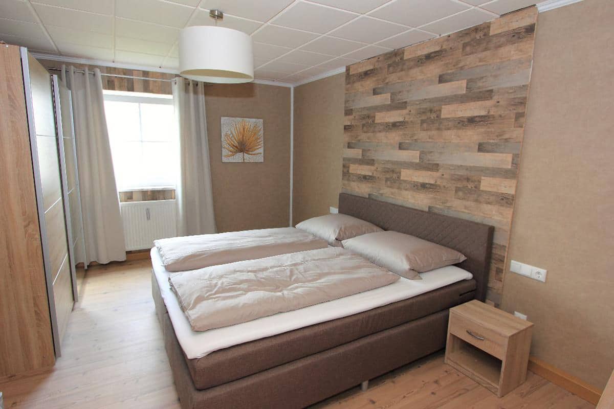 A bedroom with a double bed, a bedside table, and a wall-mounted wooden panel design.