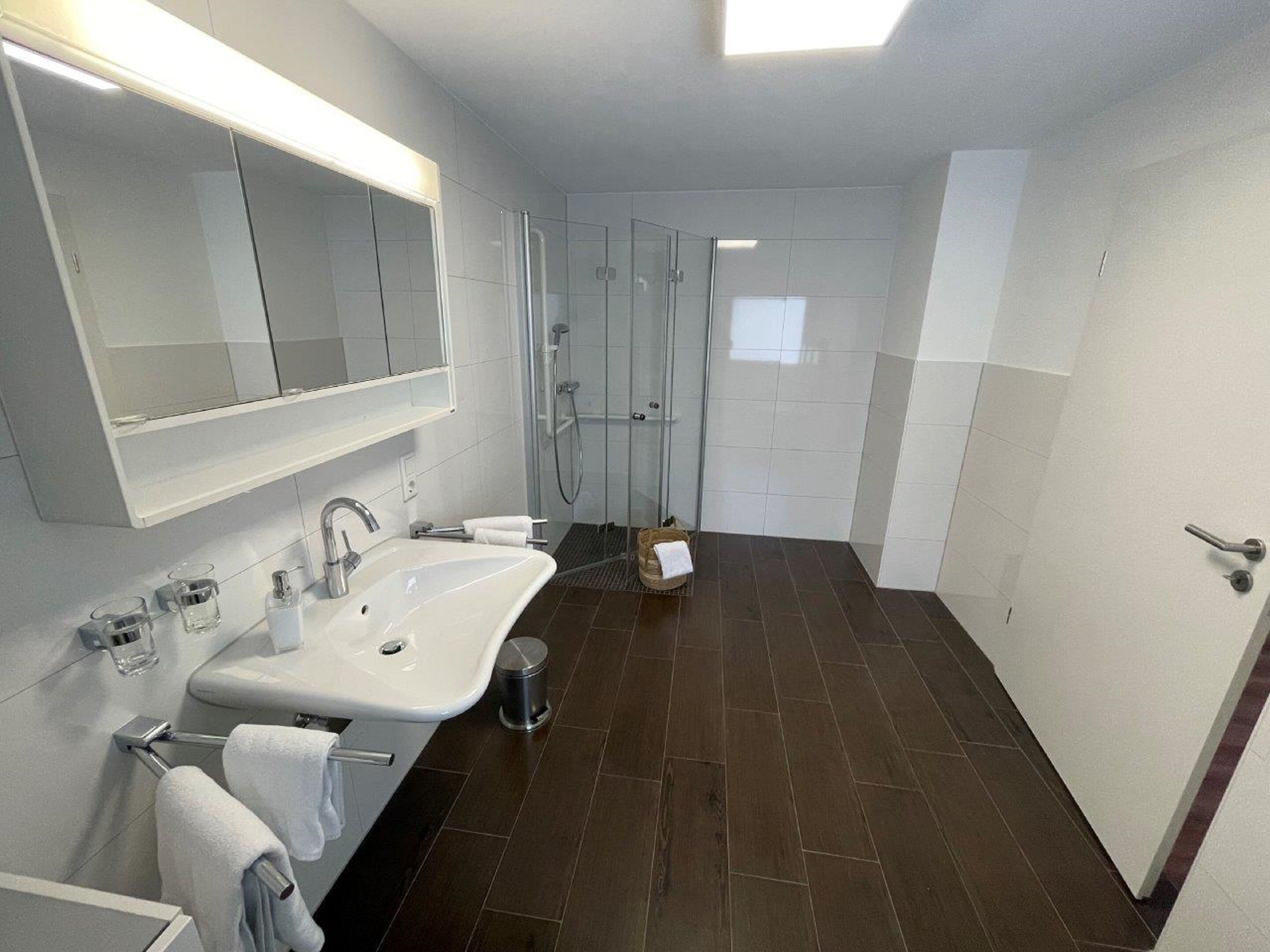A modern bathroom with a large mirror, a sink, a shower, and a toilet.