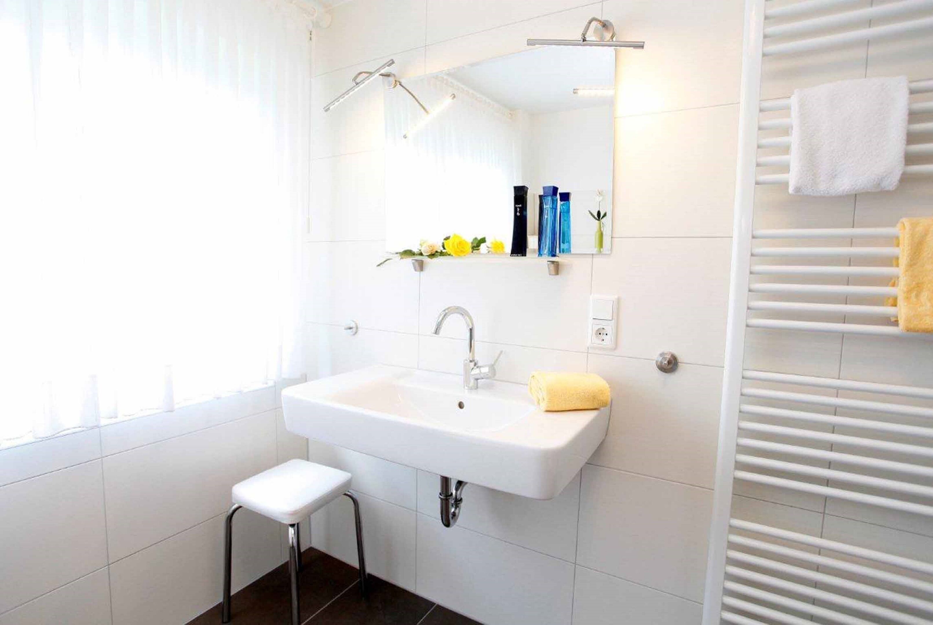 A modern bathroom with a white sink, mirror, and towel rack.