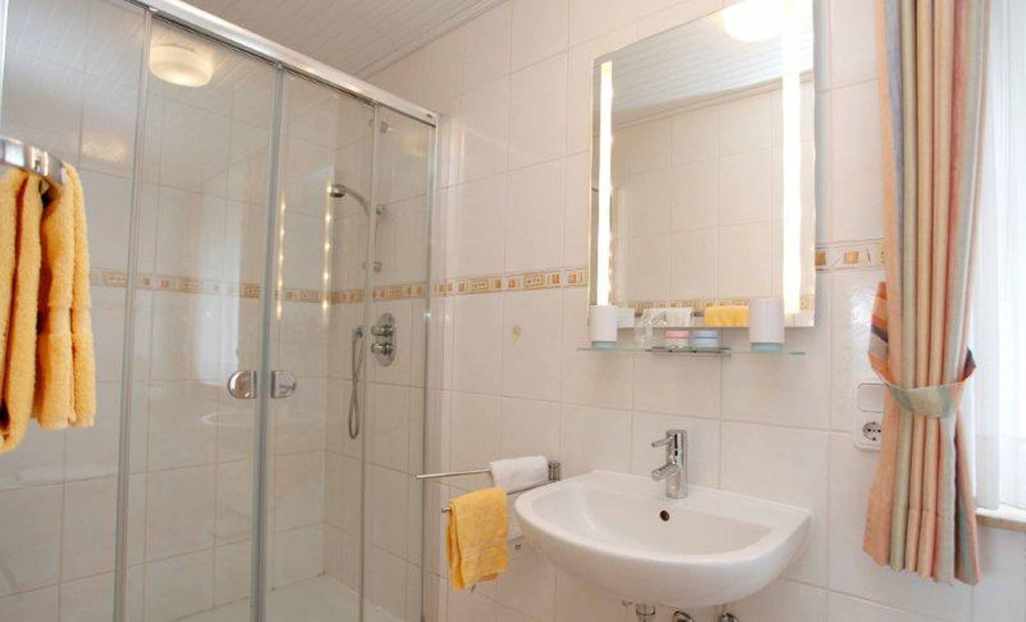 Un baño con ducha de vidrio, un lavamanos blanco y un espejo encima.