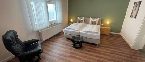 Une chambre avec deux lits, une chaise, un radiateur et une fenêtre avec des rideaux.