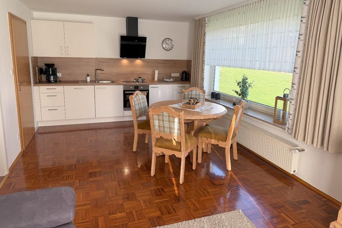 A modern kitchen with white cabinets, a black range hood, and a dining area with a round table and wooden chairs.